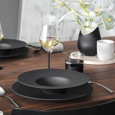 A modern wooden dining table set with Manufacture tableware A modern wooden dining table set with Manufacture tableware, wine glasses, cutlery, and a vase with white flowers.