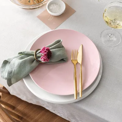 A table set with a pink Rose Garden plate, a white NewMoon plate and golden MetroChic cutlery.