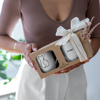 A woman holding a packaged Villeroy & Boch Statement cup set with a cat pattern.