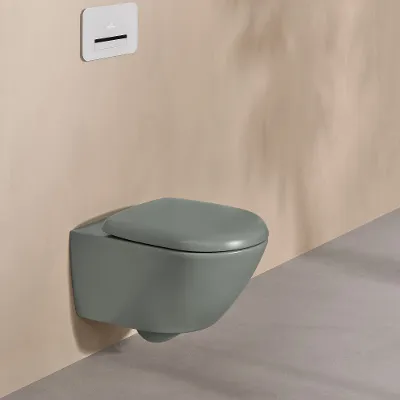 A Villeroy & Boch toilet from the Antao collection in green with a white control panel on a natural-coloured wall.