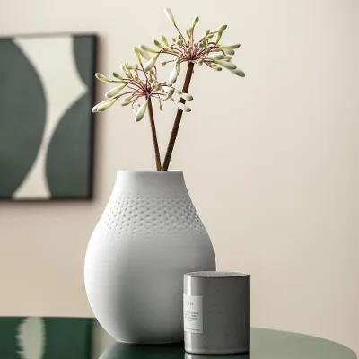 A white Manufacture vase with a subtle flower arrangement standing on a green table.