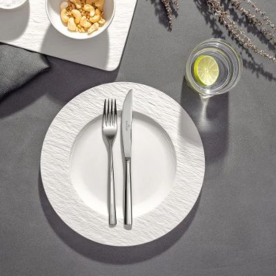A plate with a crossed fork and a knife on it, a glass of water with lime next to it and two bowls of snacks on a table.