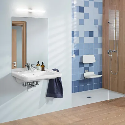 Un bagno privo di barriere architettoniche con pavimento in legno e rivestimenti in legno su una parete. Accanto al WC sono installati dei maniglioni pieghevoli e nella doccia è presente un sedile con schienale.