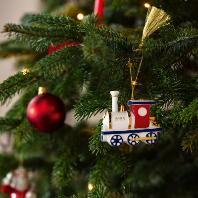 A Christmas tree adorned with a festive train ornament marked "2025" and red baubles. Warm lights add a cozy, cheerful holiday atmosphere.