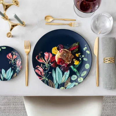 Avarua Geschirr mit MetroChic Besteck und Gourmetgericht Eleganter Esstisch mit Avarua Tellern und einem Gourmetgericht, dazu goldenes MetroChic Besteck und ein Glas Rotwein.