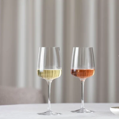 Two Villeroy & Boch Afina wine glasses are placed on a table next to a vase with pink flowers. Two Villeroy & Boch Afina wine glasses, one filled with white wine and the other with rosé, are placed on a table next to a vase with pink flowers.