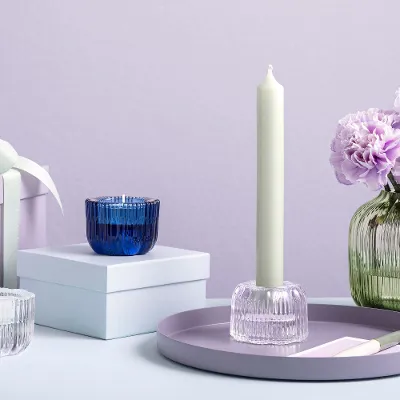 Le vase Fleur Vert de Villeroy & Boch avec des fleurs violettes est présenté sur une surface à côté de boîtes cadeau et de bougeoirs Fleur.