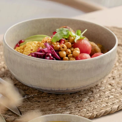 A Perlemor ceramic bowl with various vegetables A Perlemor ceramic bowl containing various vegetables, chickpeas and greens stands on a woven placemat, next to which are chopsticks.