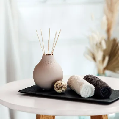 Beige Manufacture vase with fragrance sticks on a tray with towels.