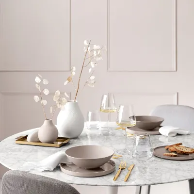 A dining table with a white table cloth and a vase of flowers, set with La Boule Pure Beige and MetroChic wine glasses.