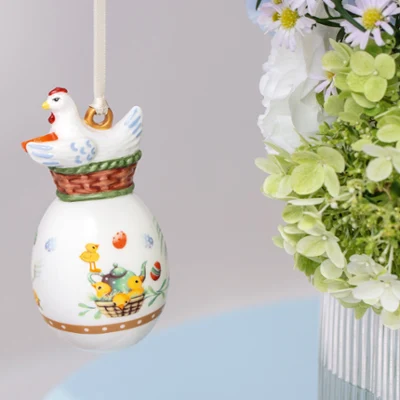Ceramic Annual Easter Edition 2026 ornament with a chicken Ceramic Annual Easter Edition 2026 ornament with a chicken design hanging near a bouquet of green and white flowers in a vase.