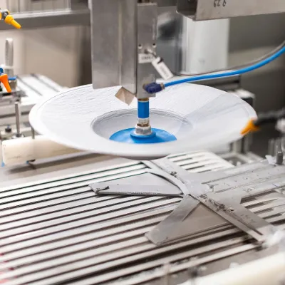 In production, a machine holds a white plate. In an automated factory environment, a machine decorates a white plate.