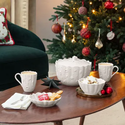 Toy’s Delight Royal Classic mugs A decorated Christmas tree with red ornaments stands behind a coffee table set with mugs, cookies, and festive decorations in a cozy living room.