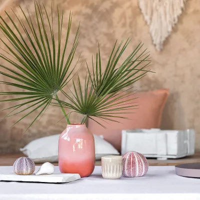 A table with a like. by Villeroy & Boch Perlemor vase and scented candle along with some shells.