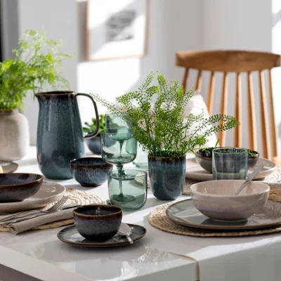 Ein schön gedeckter Esstisch mit Lave-Geschirr, Gläsern, Grünpflanzen und frischen Backwaren in einer modernen Küche von Villeroy & Boch.
