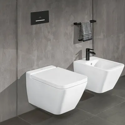 Weiße Toilette und Bidet aus der Kollektion Finion Ein modernes Badezimmer mit einer weißen wandmontierten Finion-Toilette und einem weißen Bidet. Über der Toilette befindet sich eine schwarze Spülplatte und über dem Bidet ein schwarzer Handtuchhalter mit einem grauen Handtuch an einer grau gefliesten Wand.