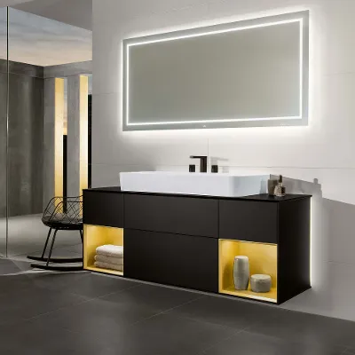 A Finion washbasin with an illuminated vanity unit and illuminated mirror in a dark-coloured bathroom.