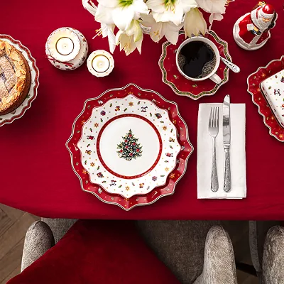 Tavola imbandita a festa con tovaglia rossa, piatto natalizio, torta, caffè e posate su tovagliolo.