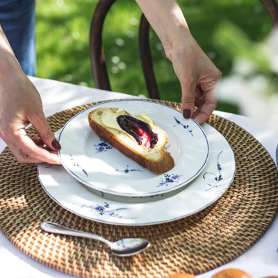 A person placing an Old Luxembourg plate on a table A person placing an Old Luxembourg plate, with fruit spread and butter, on a woven placemat.