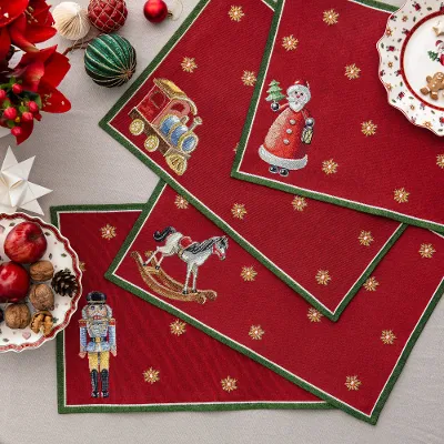 Red placemats with Christmas motifs on a round table with festive plates, cookies, fruit, nuts, and ornaments.