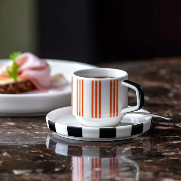 Memphis od Villeroy & Boch idealny do espresso Paskowana filiżanka do espresso Memphis na spodku stoi na marmurowym stole, obok talerza Memphis.