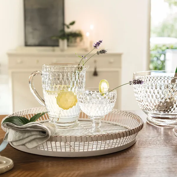 Glasses from Villeroy & Boch with lemon water stand on a tray on a wooden table with glass bowls and a napkin.