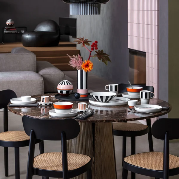 Memphis meets Design Dining table with black chairs, brightly patterned Memphis tableware, Memphis vases with flowers and contemporary decor in a modern space.