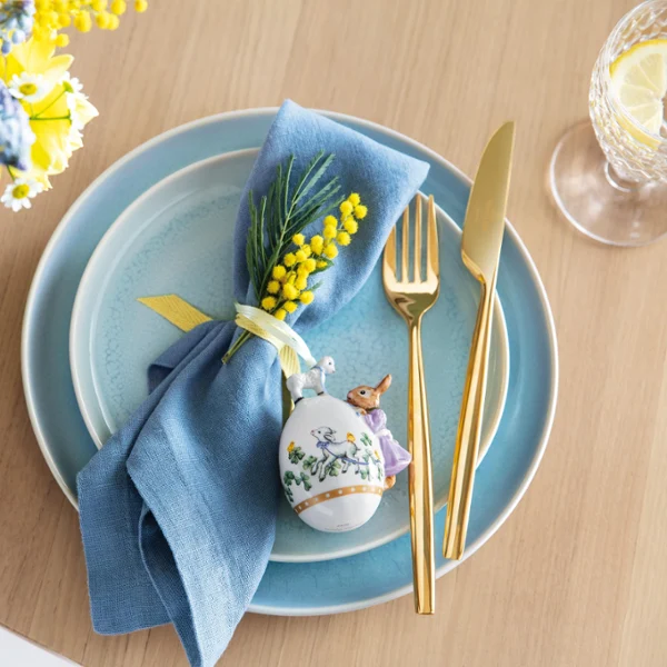 An elegantly set table with blue Crafted dinnerware and a decorative egg from the Annual Easter Edition 2022 as well as a springtime flower arrangement.