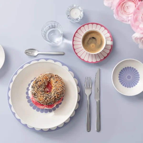 A breakfast set with bagel, cup of coffee, decorative plates, cutlery and flowers on a light blue background. A breakfast set with bagel, cup of coffee, decorative plates, cutlery and flowers on a light blue background.