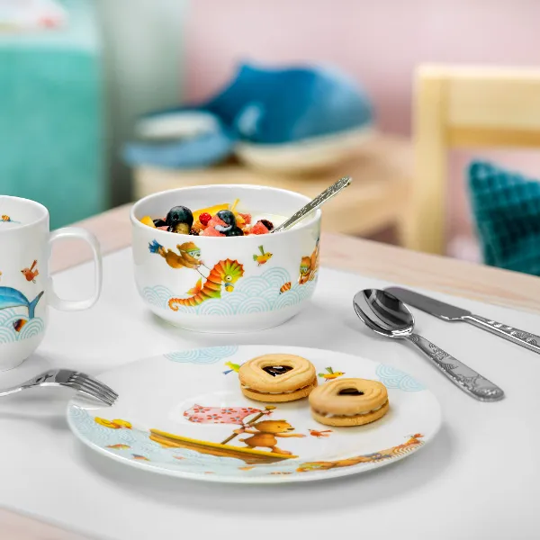 De la vaisselle pour enfants Happy as a bear avec de la salade de fruits et des biscuits Une présentation de petit-déjeuner avec une salade de fruits, des biscuits sur une assiette et deux tasses de vaisselle pour enfants Happy as a bear sur une table.