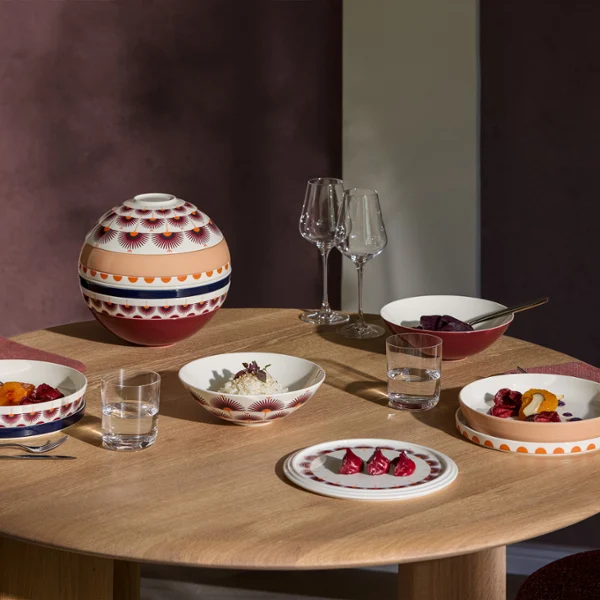 La Boule Kyoto tablesetting with food Una mesa redonda de madera, puesta con vajilla estampada de La Boule Kyoto, vasos y un cuenco con tapa, lista para una comida para tres personas.