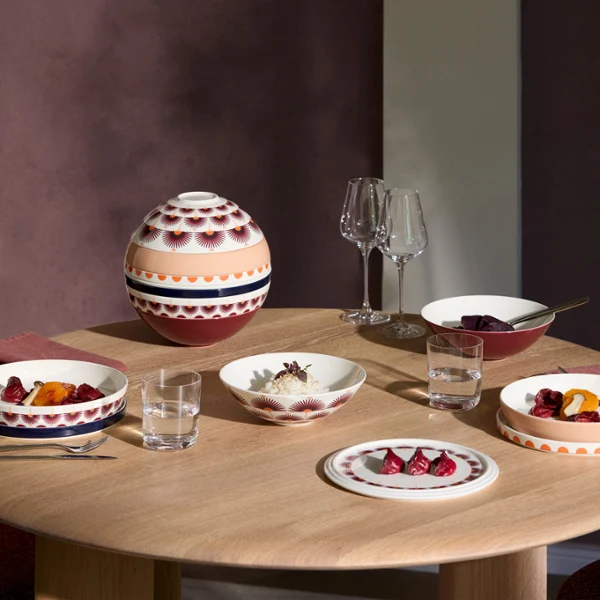 La Boule Kyoto tablesetting with food A round wooden table set with patterned tableware from La Boule Kyoto, glasses, and a bowl with a lid, ready for a meal for three.