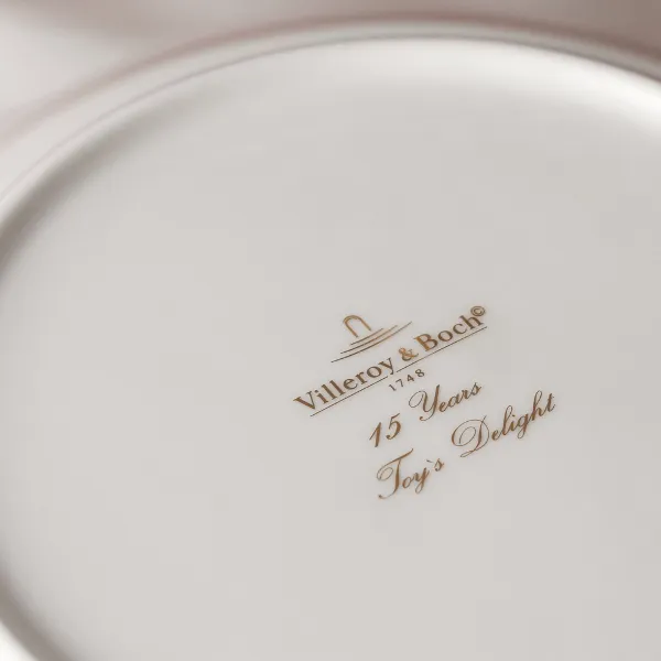 The underside of a white Villeroy & Boch plate with gold lettering and the inscription "15 Years Toy's Delight." 