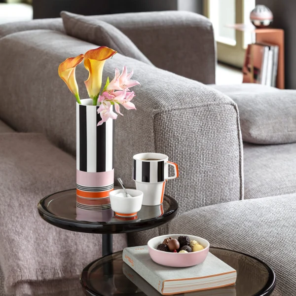 Deux tables basses rondes avec un vase à fleurs Memphis, une tasse à café Memphis, un sucrier, un livre et un bol de chocolats dans un salon moderne.