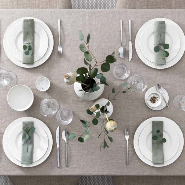 Elegantly set dining table with harmonious, white Manufacture dinnerware and glasses Elegantly set dining table with matching dinnerware and glasses from the Manufacture collection in white and a simple green and white centerpiece.