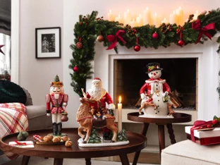 Living room decorated for Christmas with garlands, candles, figures and wrapped presents next to a fireplace and a coffee table.