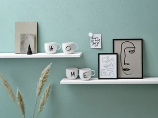 Minimalist shelves with decoration objects, including cups with the word "Home", a framed abstract painting of a face and a potted plant.