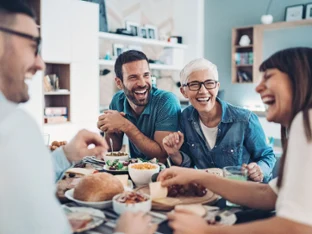Four laughing people are sitting at a set table in the dining room