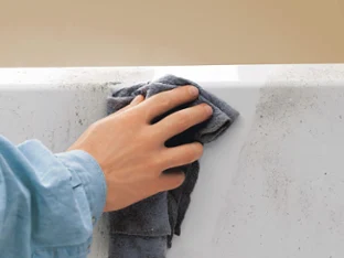 A person in a blue shirt using a dark cloth to remove dirt from a white Quaryl bath.