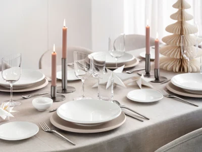 NewMoon crockery on a table A dining table with white plates, glasses, candles and paper decorations on a neutral tablecloth.