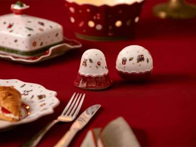 Salt and pepper shakers Salz- und Pfefferstreuer mit Weihnachtsmotiv auf einer roten Tischdecke, umgeben von festlichem Geschirr und einem Gebäckstück.