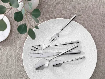 Elegante Tischdekoration mit modernem Piemont Besteck und dekorativem Grün auf einer neutralen Tischdecke.