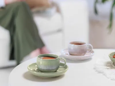 L’heure du café avec Perlemor dans un salon confortable Deux tasses à café Perlemor sur une table de salon, avec en arrière-plan une personne partiellement visible sur le canapé.