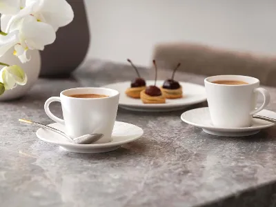 Manufacture Rock blanc Espressotasse mit Gebäck Zwei Manufacture Espressotassen und ein Teller Gebäck auf einem Marmortisch mit Orchideen im Hintergrund.