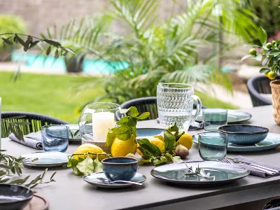 Esstisch im Freien mit Lave Geschirr, Gläsern, Kerzen und frischen Zitrusfrüchten als Tafelaufsatz mit Blick auf einen Pool.