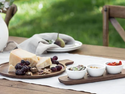 They are served with three small dip bowls containing sliced vegetables, nuts, and sun-dried tomatoes. Artesano wooden board from Villeroy & Boch, decorated with cheese, grapes, walnuts, and figs. They are served with three small dip bowls containing sliced vegetables, nuts, and sun-dried tomatoes.