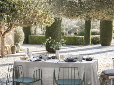 Boston Smoke glasses and Lave crockery on an outdoor table setting Outdoor dining area under trees with Lave plates on the table accompanied by elegant dark Boston glasses and Boston cutlery on a pebble surface.