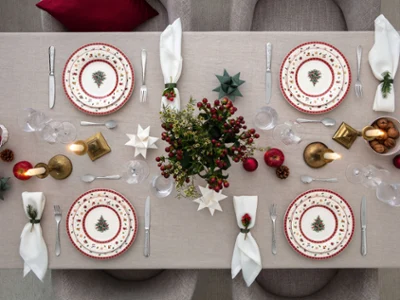 Toy's Delight festive grey table setting Overhead view of a grey table set for Christmas with Toy's Delight plates, white napkins, lit candles, apples, and green foliage.