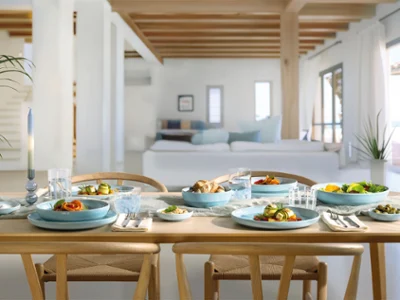 A wooden dining table for four people with blue Perlemor Aqua plates A wooden dining table for four people with blue Perlemor Aqua plates in a bright, modern living area.