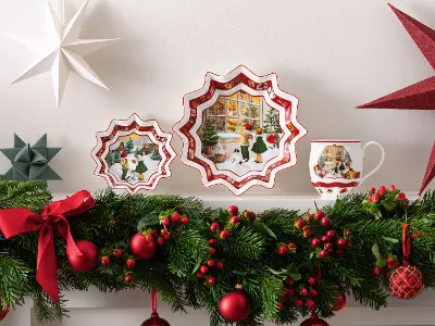 Toy’s Fantasy-Kollektion von Villeroy & Boch Toy’s Fantasy-Kollektion von Villeroy & Boch, ein dekorativer Teller, ein mit Winterlandschaften verzierten Becher, sternförmige Ornamente und eine üppige, mit roten Bändern und Beeren geschmückte Girlande auf dem Kaminsims umfasst.